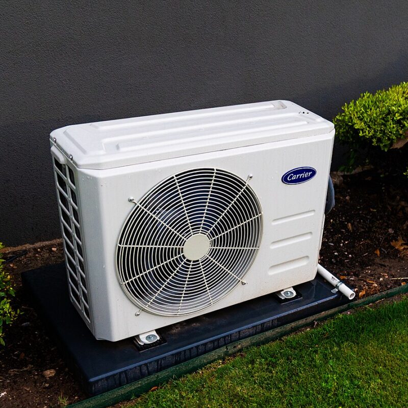 Carrier outdoor AC heat pump condenser unit mounted on a pad beside a home with green shrubs